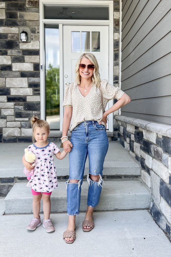 Cute mom outfit with distressed jeans and a neutral polka dot blouse.