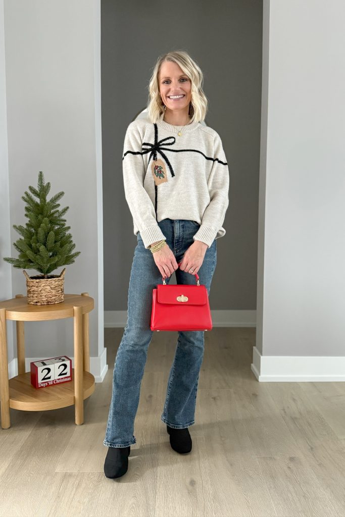 holiday bow sweater with flare jeans and red purse