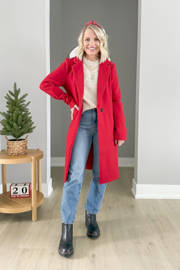 Woman in a red coat, cream sweater, and jeans, styled with black boots and a plaid headband.