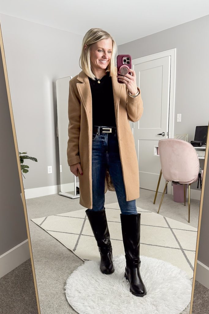 Mirror selfie in a camel coat with a black top, skinny jeans and black tall riding boots.