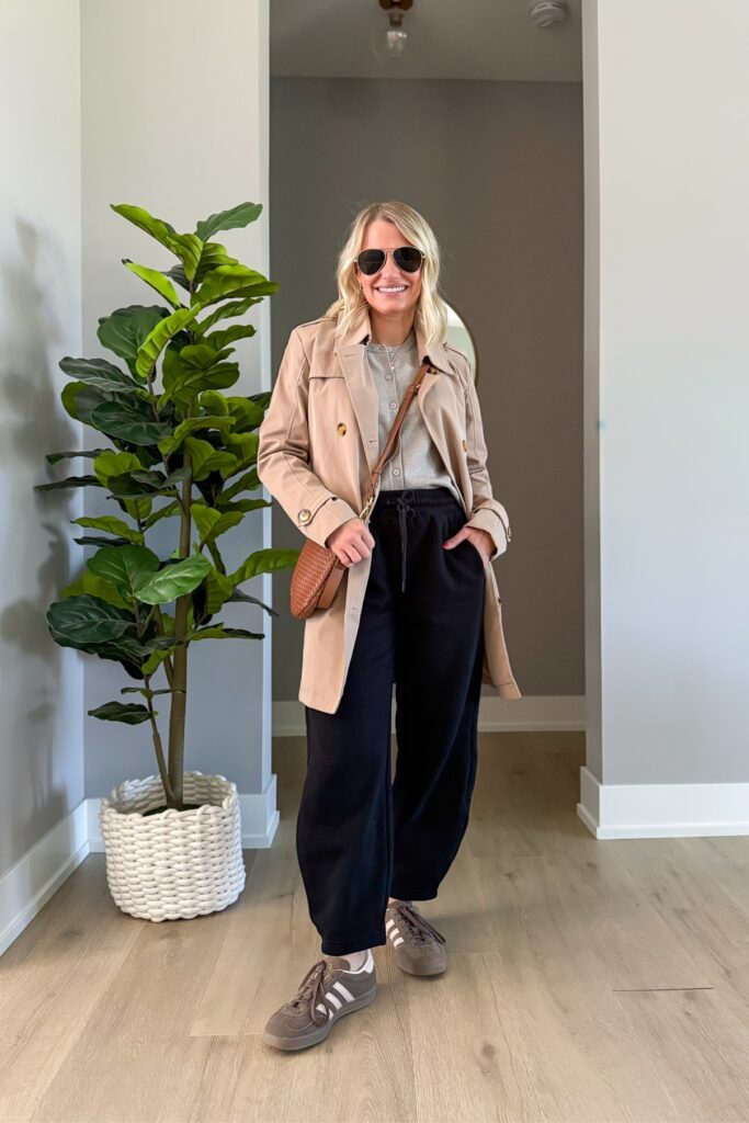 Tan trench coat over a gray cardigan and black drawstring pants with sunglasses, a brown woven crossbody bag, and sneakers
