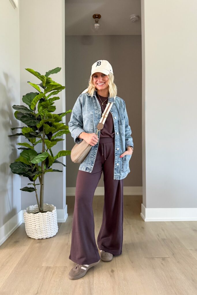 Oversized denim jacket over a brown lounge set with a cream baseball cap, a woven crossbody bag, and sneakers